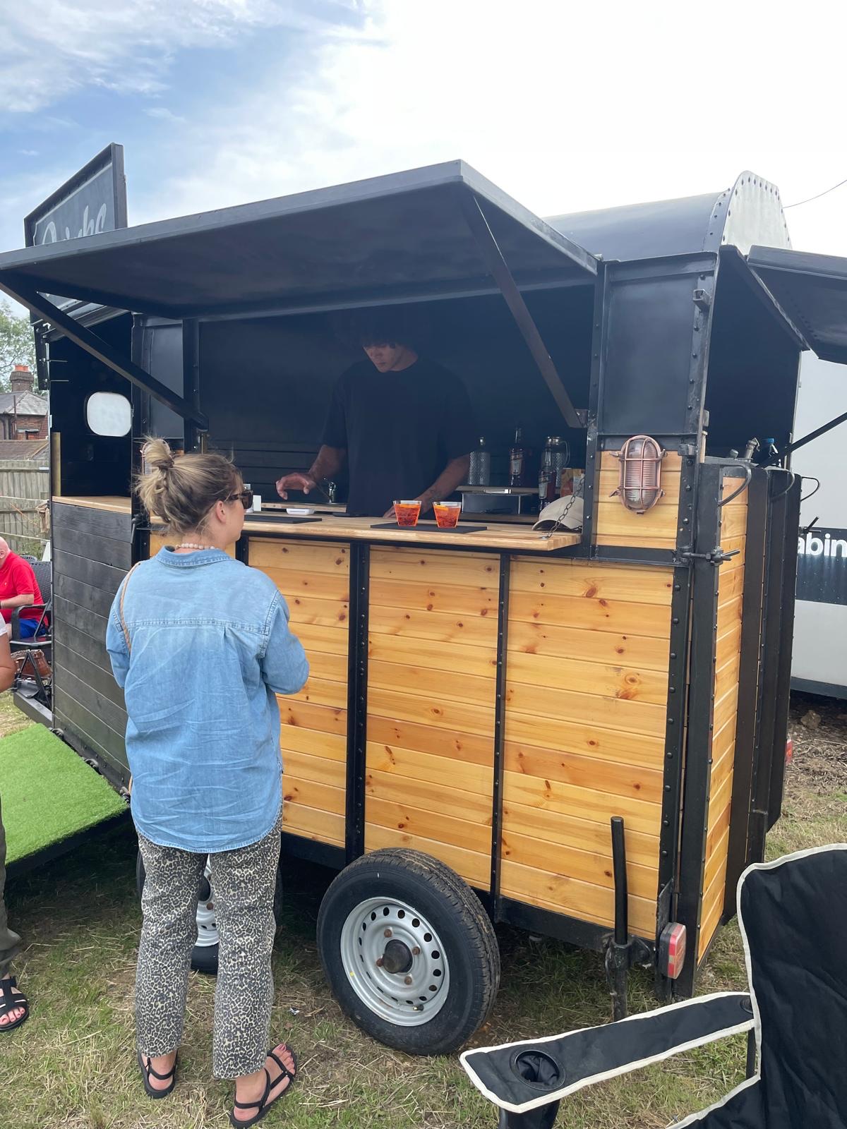 The Box trailer with the hatch open, serving two drinks from the pine counter