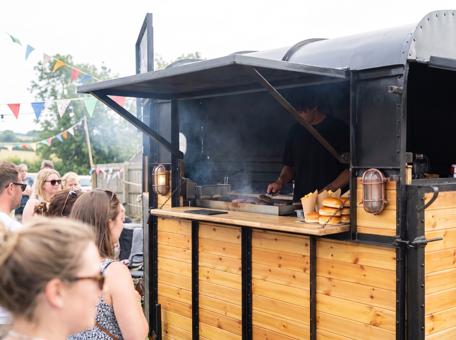A chef cooking burgers on a flat-top grill inside The Box at a festival